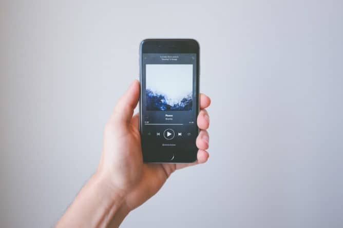 在分散的媒体环境中，一只手拿着一部智能手机，上面播放着音乐。